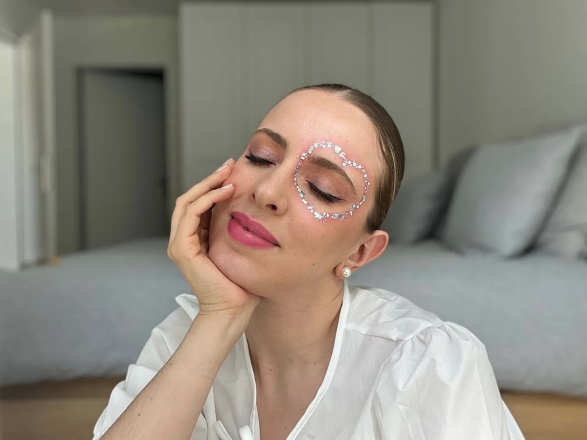 Frau präsentiert Make-up-Look passend zu Lovers für die Taylor Swift Eras Tour mit einem Glitter-Herz ums linke Auge